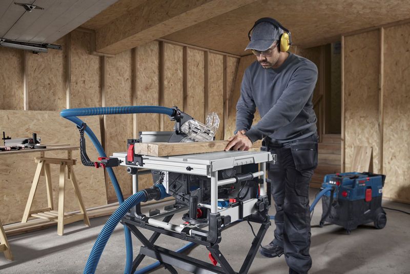 A person wearing safety equipment makes a wood cut using a table saw in a workshop.