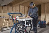 A person wearing safety equipment makes a wood cut using a table saw in a workshop.