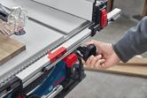 A person adjusts a table saw fence using a black knob in a workshop.