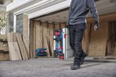A person wearing safety equipment carries a portable table saw at a construction site.