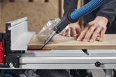 A person guides wood through a table saw with dust extraction mounted.