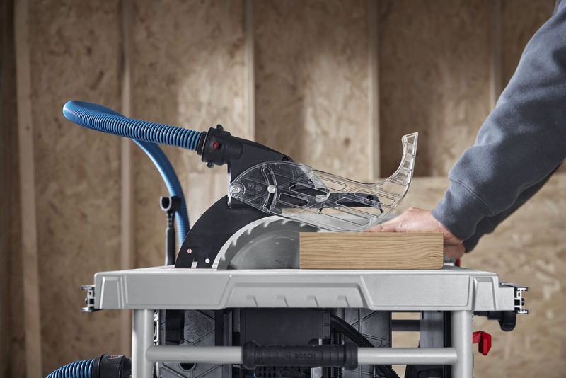 A person guides wood through a table saw in a workshop.