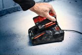 A person places a red and black battery pack onto a charging station.