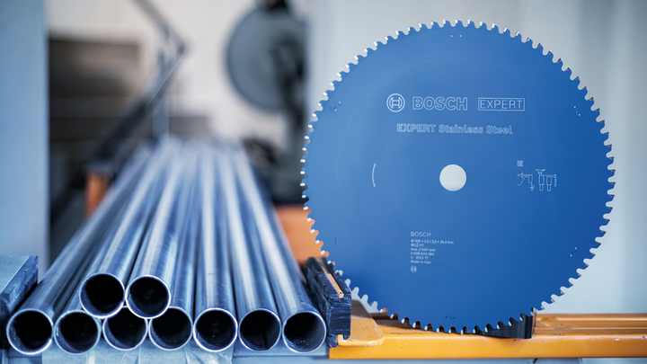 Object #200585175: 7557704_app_web_02 Circular saw blade next to stacked metal pipes on an industrial workstation.