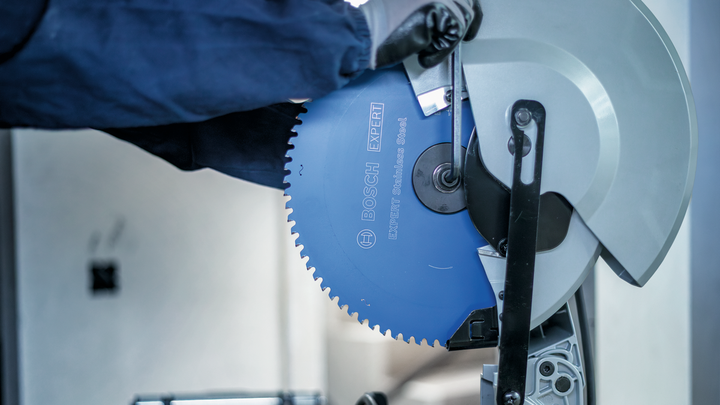 Object #200585177: 7557704_app_web_04 Person wearing safety equipment adjusts a blue circular saw blade on a metal cutting machine.