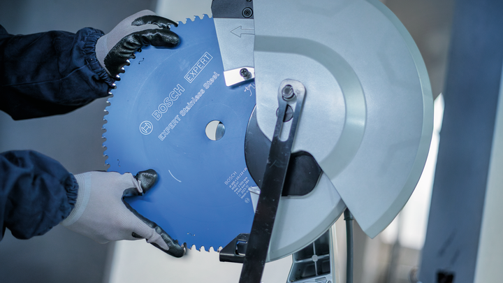 Object #200585183: 7557704_app_web_10 Person wearing safety equipment installs a circular saw blade into a metal cutting machine.