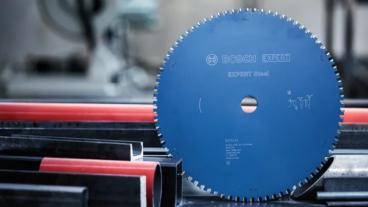 Object #200585208: 7557706_app_web_02 Circular saw blade positioned upright beside metal and plastic pipes in a workshop.