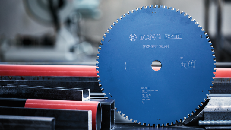EXPERT Steel Circular Saw Blade, 254 x 2.6/2.2 x 25.4 mm, T60 Circular saw blade positioned upright beside metal and plastic pipes in a workshop.