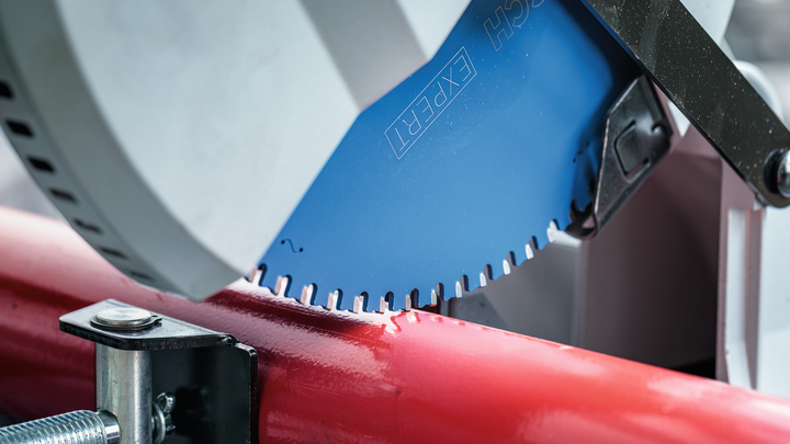 Object #200585213: 7557706_app_web_07 Circular saw blade cutting through a red metal pipe in a workshop setting.