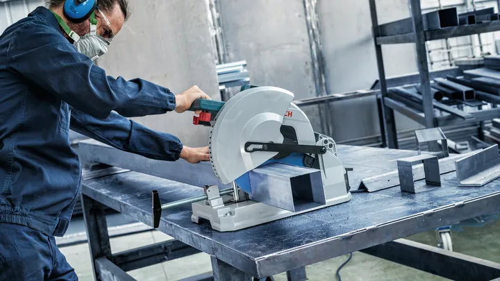 Object #200585215: 7557706_app_web_09 Person wearing safety equipment cuts a metal beam with a circular saw in a workshop.