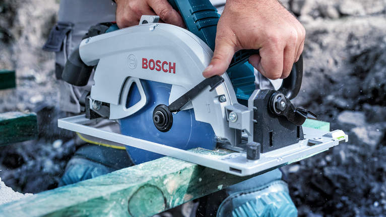 Person wearing safety equipment cuts wood with a circular saw.
