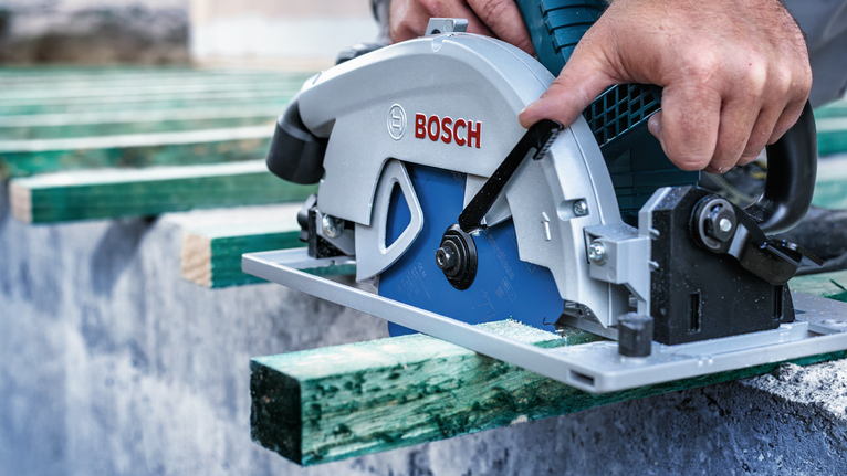 Person operates a circular saw to cut a green wooden beam.