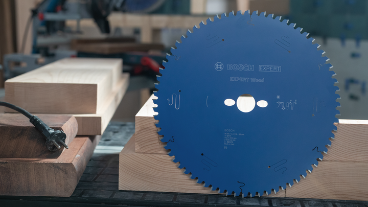 Object #200585316: 7557711_app_web_02 Large circular saw blade standing upright on stacked wooden beams in a workshop.