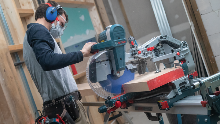 Object #200585323: 7557711_app_web_09 Person wearing safety equipment cuts a wooden plank with a sliding miter saw.