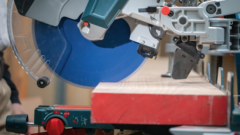 EXPERT Wood Circular Saw Blade, 250 x 2.4/1.8 x 30 mm, T60 Miter saw with a blue blade cutting a wooden plank on a workshop table.