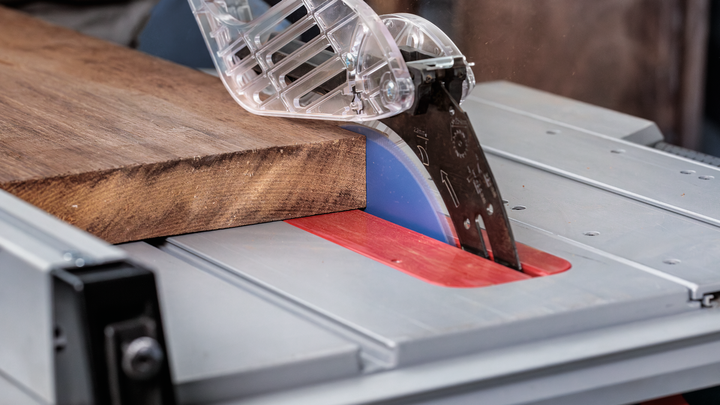 Object #200585341: 7557712_app_web_06 Circular saw cutting through a wooden board with a safety guard in place.