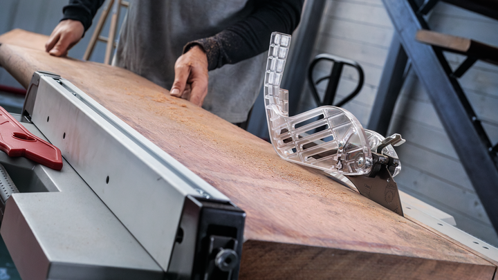 Object #200585343: 7557712_app_web_08 Person pushing a large wooden board through a table saw in a workshop.