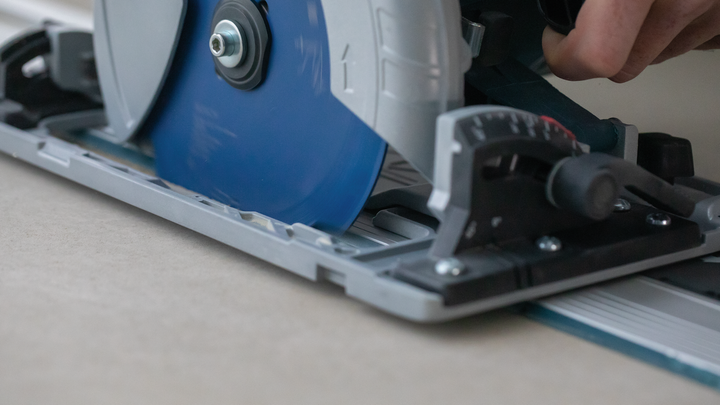 Object #200585529: 7557691_app_web_06 Person guides a circular saw along a metal track to cut a sheet of wood.