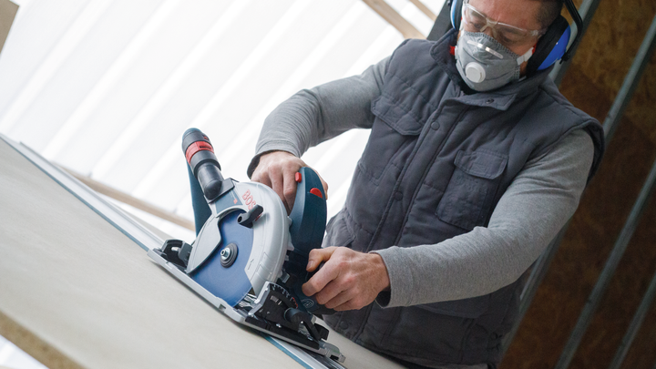 Object #200585532: 7557691_app_web_09 Person wearing safety equipment uses a circular saw to cut a sheet of material.