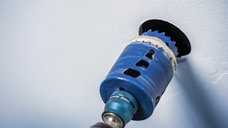 Power tool with a hole saw attachment drilling a circular opening in a wall.