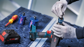 Person wearing safety equipment attaches a drill bit to a cordless power tool.