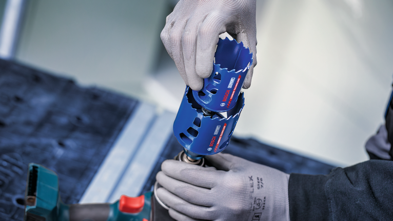 Person wearing safety equipment attaches a blue hole saw to a power tool.