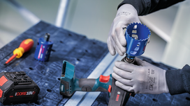 Person wearing safety equipment attaches a hole saw to a cordless drill on a workbench.