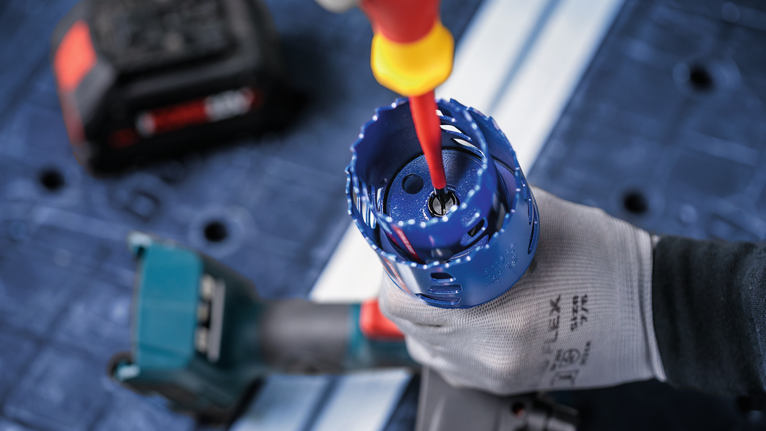 Person wearing safety equipment adjusts a hole saw attached to a power drill.