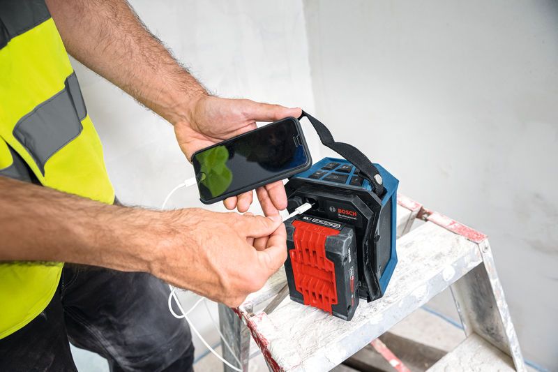 GPB 18V-1 C A person wearing safety equipment connects a smartphone to a portable Bluetooth speaker on a ladder.