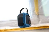 Blue Bluetooth speaker with carry handle placed on a windowsill at a construction site.