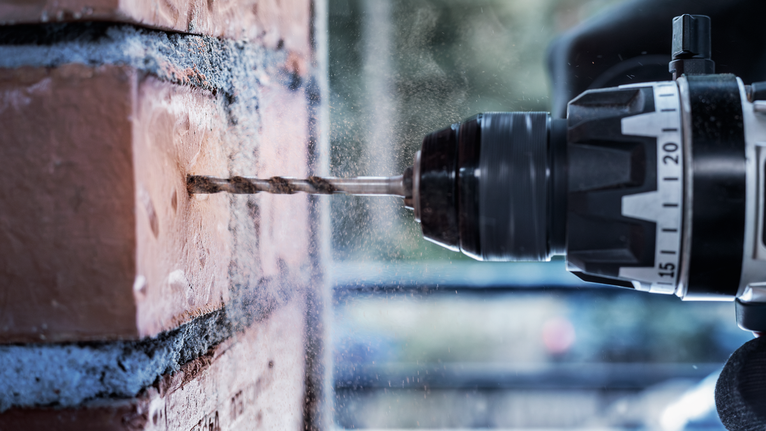 Drill making a hole in a brick wall, dust scattering from the surface.