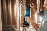 A person wearing safety equipment drills through a wooden stud with a cordless angle drill.
