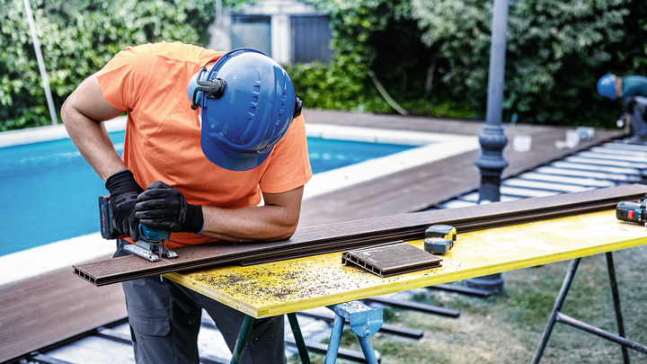 Person wearing safety equipment uses a jigsaw to cut decking boards outdoors.