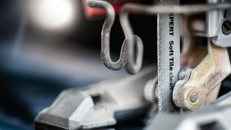Jigsaw blade cutting through tile at a close angle.
