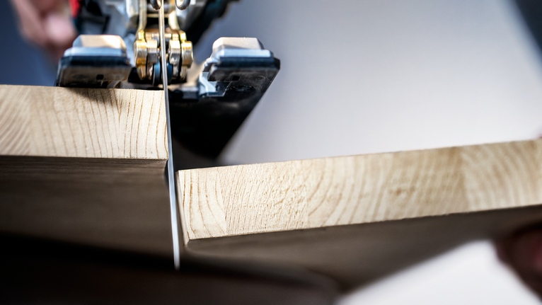 A person cuts a wooden board with a jigsaw.