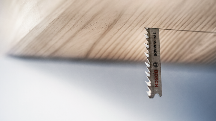 Jigsaw blade cutting through a wooden board from below.