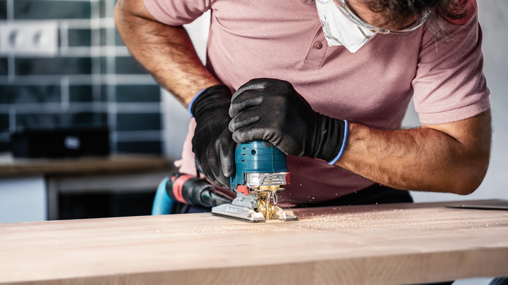 A person wearing safety equipment uses a jigsaw to cut wood.
