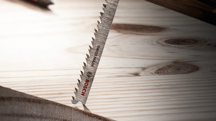 Jigsaw blade cutting through a wooden board.