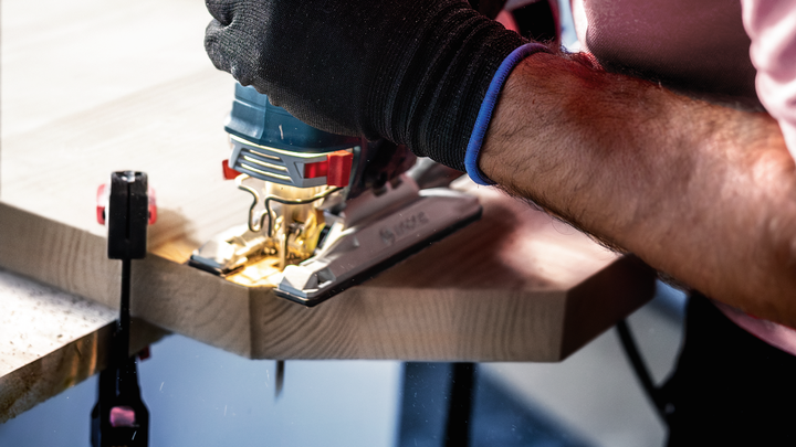 Person wearing safety equipment cuts a wooden plank with a jigsaw.