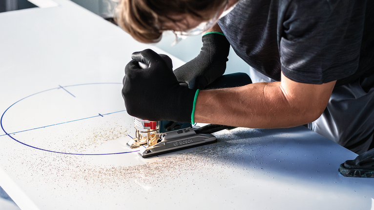 EXPERT Hardwood 2-side clean T308BFP Jigsaw Blade, 3 pcs Person wearing safety equipment uses a jigsaw to cut a curve in a marked board.