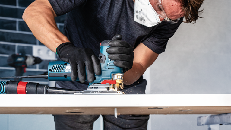 EXPERT Hardwood 2-side clean T308BFP Jigsaw Blade, 3 pcs Person wearing safety equipment uses a power jigsaw to cut a wooden board.