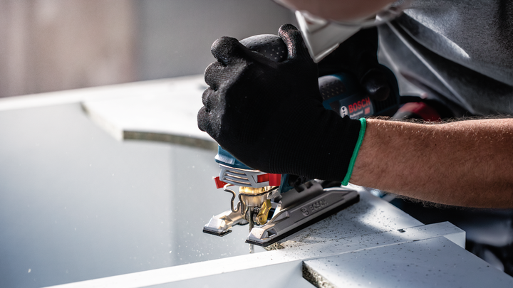 Object #200597896: 2793300_app_web_01 Person wearing safety equipment uses a jigsaw to cut a sheet of material.