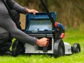 A person adjusts the grass collector on a cordless lawnmower outdoors.