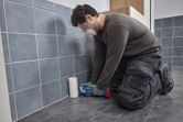 A person wearing safety equipment uses a multifunction tool to cut floor tiles.