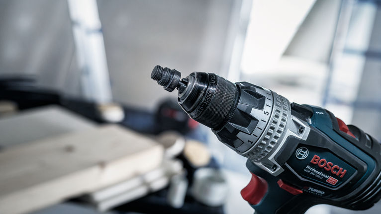 Cordless drill with a metal chuck in focus in a workshop setting.