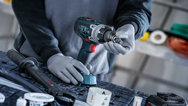 Person wearing safety equipment inserts a drill bit into a cordless power drill.