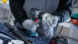 Person wearing safety equipment attaches a hole saw to a cordless drill.