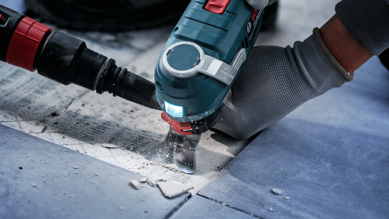 Person wearing safety equipment uses a power tool to cut tiles.