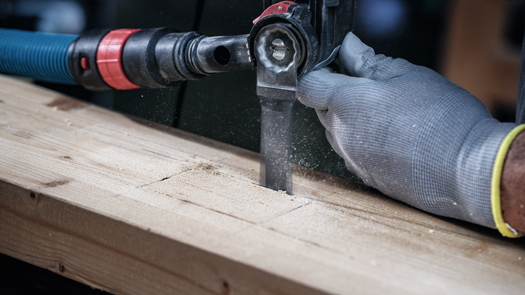 Person wearing safety equipment cuts a wooden plank with a reciprocating saw.