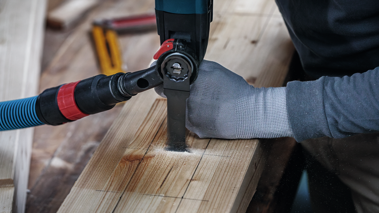 Person wearing safety equipment uses a power saw to cut a slot in a wooden plank.